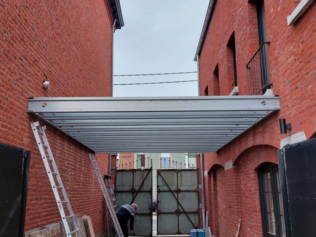 Installation d’une ossature de terrasse en acier ModuHome entre deux bâtiments en briques.