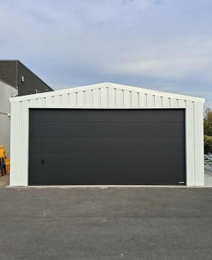 Garage ModuHome en ossature métallique légère avec porte sectionnelle noire.